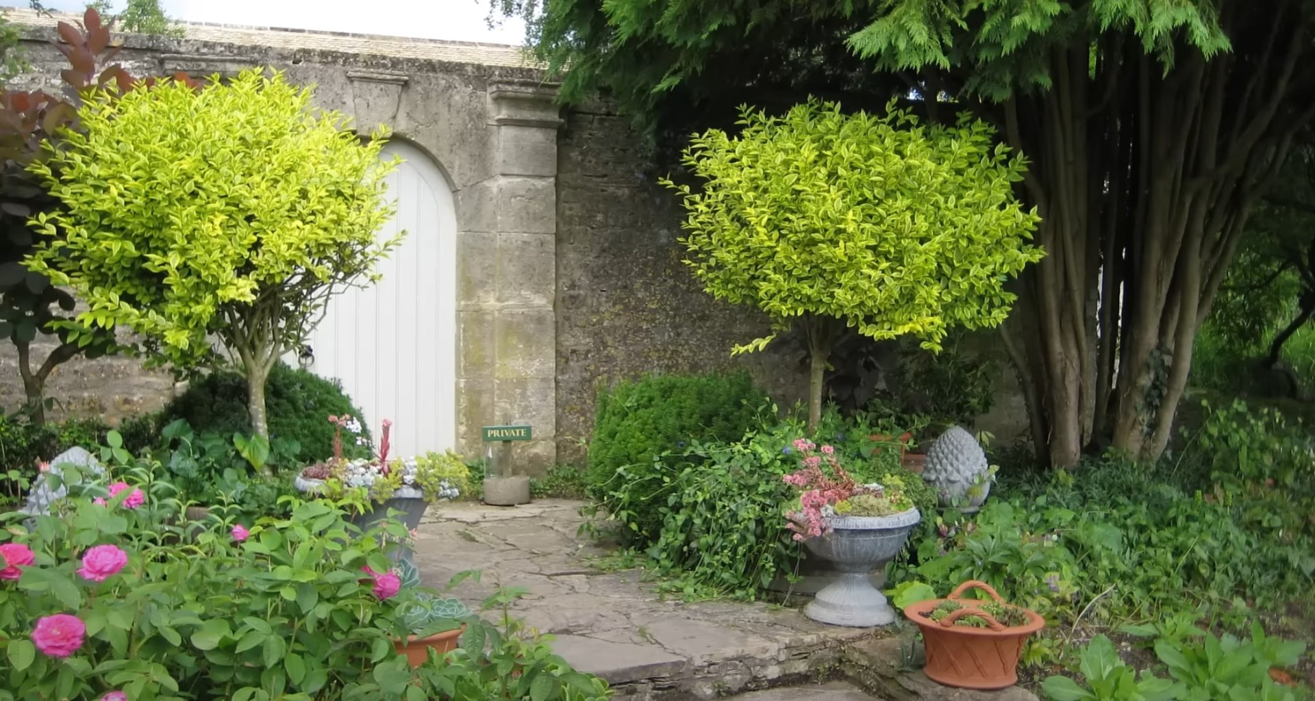 Traditional landscape design with stone features and seasonal flower plantings Charming garden entrance with stone archway, colorful flowers, and established shrubs