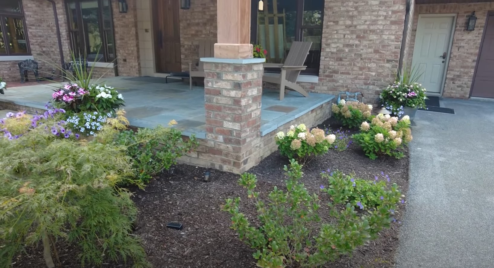 Professional front entrance landscaping with architectural elements and seasonal maintenance Elegant front entrance landscaping with brick columns and seasonal flower displays