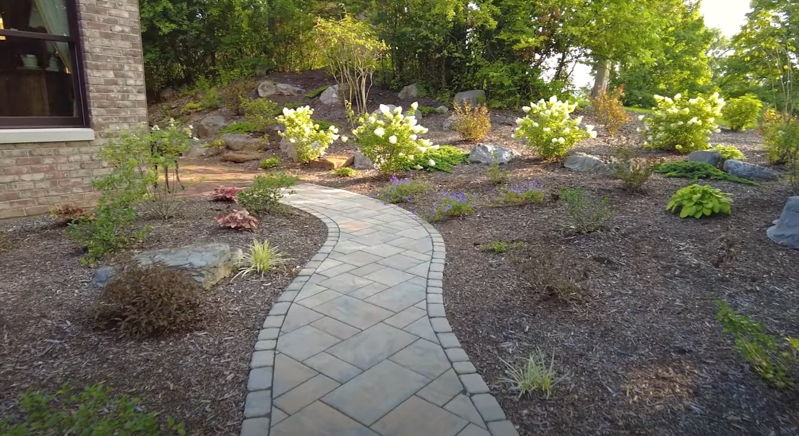 Hardscaping installation featuring curved walkways and seasonal landscape maintenance Curved stone pathway through professionally designed landscape beds with flowering shrubs